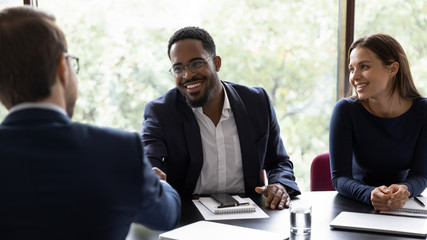 Wall Mural - Smiling African American male employee shake hand of colleague greeting getting acquainted at office meeting, happy diverse businessman handshake close deal after successful negotiations at briefing