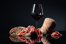 Prosciutto With Ciabatta, Red Wine And Thyme On A Black Background.
