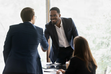 Wall Mural - Smiling multiracial male business partners handshake greeting getting acquainted at office meeting, happy divers multiethnic man colleagues shake hands close deal or make agreement at briefing