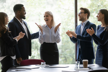 Overjoyed diverse businesspeople applaud celebrate company business success at meeting together, happy multiracial employees clap hands congratulate middle-aged businesswoman, reward concept