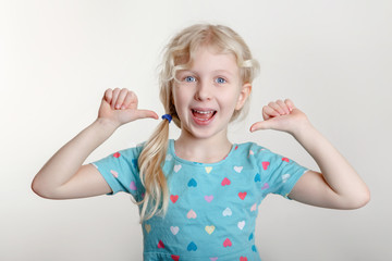 Wall Mural - Portrait of beautiful little funny joyful blonde Caucasian girl on a light background. Happy smiling preschool child kid showing like thumb fingers. Positive emotion face expression.