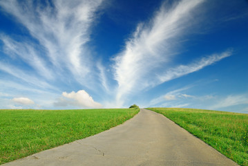 landscape, dirty road among green fields, blue sky in the backgr