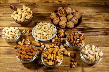 Sticker - Assortment of nuts on wooden table. Almond, hazelnut, pistachio, peanut, walnut and cashew in small bowls. Healthy eating concept