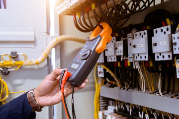 Electrician measurements with multimeter testing current electric in control panel.