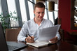 © Konstantin Zibert - Young businessman wearing a white fashion shirt sittting in a cafe with a laptop, documents and writing in notebook. Freelance and selfemployment concept. Distance job.
