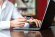 © Konstantin Zibert - Closeup of hands of young businessman wearing a white fashion shirt with a credit card and laptop making payment online in a cafe. Freelance and selfemployment concept. Distance job.