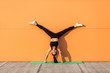 © khosrork - Glad happy humorous girl with perfect athletic body in tight sportswear doing yoga handstand pose with spread legs against wall and showing tongue, having fun. Gymnastics for body balance, flexibility