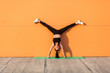 © khosrork - Overjoyed happy girl with perfect athletic body in tight sportswear doing yoga handstand pose with spread legs against wall and showing tongue, having fun. Gymnastics for body balance, flexibility