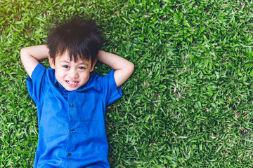 Portrait of cute happy smiling little asian boy child lying on green grass outdoors.Kid felling relaxing and enjoy time with copy space for adding text in summer park