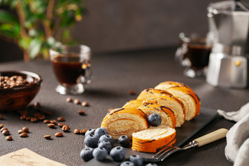 Wall Mural - Sweet roll with cream and blueberries on a board on a dark background