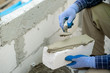 © visoot - Plastering the wall.Hand holding a spatula with construction mix.Applying putty or tile glue to with lightweight concrete blocks.Plaster the wall with a putty knife.Internal construction.