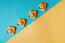 Four Yellow Rubber Ducks On A Blue And Yellow Background. Bath Concept. Copy Space, Flat Lay.