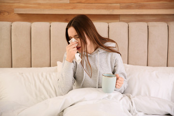 Poster - Sick young woman with cup of hot drink in bed at home. Influenza virus