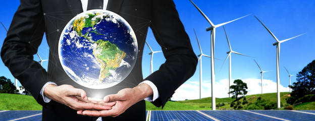 Concept of sustainability development by alternative energy. Man hand take care of planet earth with environmentally friendly wind turbine farm and green renewable energy in background.