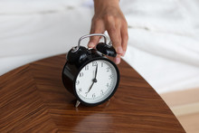 Close Up Of Female Hand Touch Clock Turn Off Wind-up Alarm Waking Up In Morning In Cozy White Bed, Woman Awaken At Home Bedroom Switch Signal Ringing, Rest And Relaxation Concept
