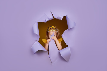 cute little child girl in princess costume breaks through a colored purple paper wall. points with a