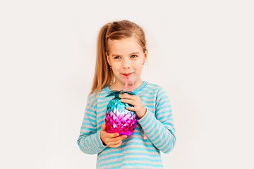 Little blonde girl is smiling on a white background. child girl in a blue jacket is holding a pineapple-shaped drink glass on a white background. summer vacation concept