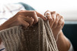 © fizkes - Close up of mature 60s grandmother hold knitting needles engaged in favorite hobby at home, elderly retired 50s woman knit sweater or scarf enjoy weekend leisure activities indoors