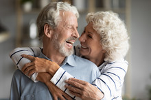 Happy Elderly Retired 60s Husband And Wife Hug Cuddle Look In Eyes Share Close Tender Moment Together, Smiling Overjoyed Old Mature 50s Couple Embrace Show Love, Care And Affection Enjoy Time At Home