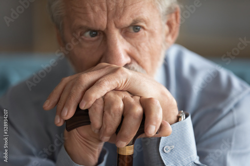 Close up of sad distressed mature 60s man with walking stick look in distance thinking pondering, upset lonely old male with wooden cane lost in thoughts yearning or missing, elderly solitude concept