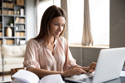Fototapeta na szkło Przewodzi strzał przyjemnego szczęśliwego młodej kobiety freelancer pracuje na komputerze w domu. Atrakcyjna bizneswoman studiuje online, korzysta z oprogramowania laptopa, surfuje po Internecie lub robi zakupy w sklepie internetowym.