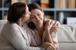 Kind loving senior mature mother feeling happy after calming young daughter, sitting together on couch. Affectionate middle aged mom kissing embracing pleasant peaceful grownup child at home.