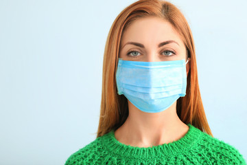 Wall Mural - Young woman with protective mask on light background. Concept of epidemic