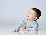 Little baby boy toddler in grey casual jumpsuit and barefoot lying on floor, smiling and looking up