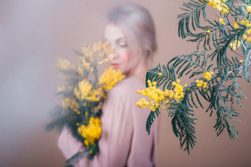 Mystical woman from the fairy tale with bouquet of mimosa flowers. Selective focus in mimosa.