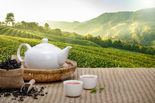 Warm Cup Of Tea With Teapot, Green Tea Leaves And Dried Herbs On The Bamboo Mat At Morning In Plantations Background With Empty Space, Organic Product From The Nature For Healthy With Traditional