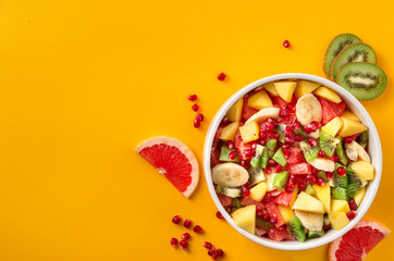 Healthy colourful fruit salad in bowl on yellow background with copy space top view Diet summer food concept