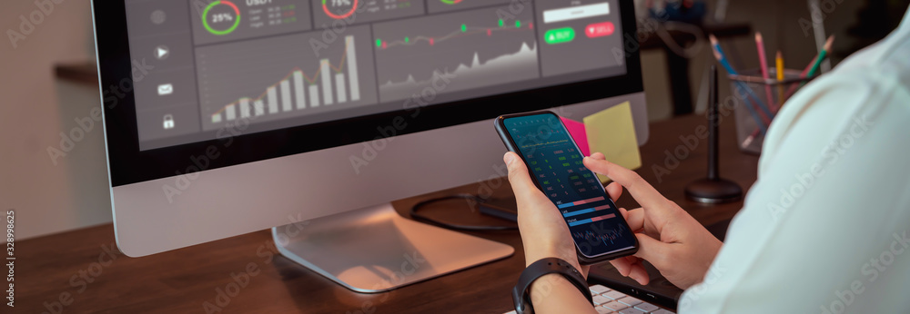 Stock exchange market concept, businesswoman trader looking on smartphone and computer with graphs analysis candle line on table in office, diagrams on screen. proportion of the banner for ads. - obrazy, fototapety, plakaty 