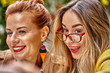 © afefelov68 - A middle-aged red-haired woman in a brown coat and a brown-haired young woman in a yellow coat and with glasses  are sitting in a summer street cafe and choose food and drinks from the menu.
