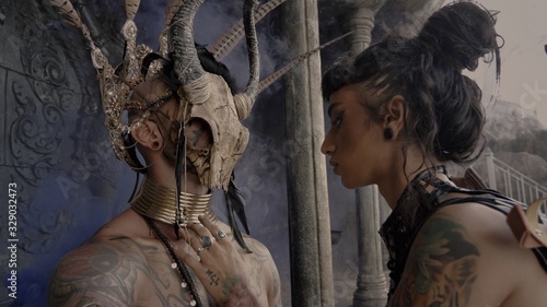 Adventure scene.Girl in a tomb raider style with sword near Tattooed masked skull ethnic pagan shaman at ancient temple