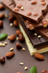 Wall Mural - sweets, confectionery and food concept - bars of dark, white and milk chocolate with nuts on brown background