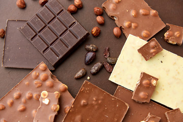 Wall Mural - sweets, confectionery and food concept - milk, dark and white chocolate bars with hazelnuts and cocoa beans on brown background