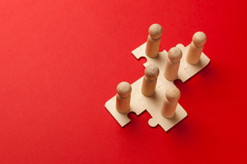 wooden figures on puzzles on red background as a symbol of team building. organization group people 