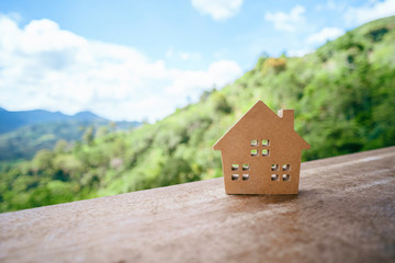 Small model home on wooden table with mountain view and blue sky white cloud abstract background.