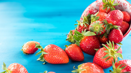 fresh bright strawberries spilled out of the bowl on a blue background