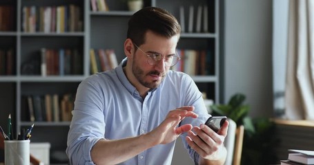 Wall Mural - Male millennial professional holding modern smartphone texting message in office. Young businessman using helpful mobile apps for business time management organization concept sitting at work desk.