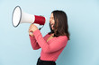 © luismolinero - Young mixed race woman isolated on blue background shouting through a megaphone