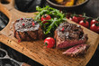 Grilled fillet steaks on wooden cutting board. Succulent thick juicy portions of grilled fillet steak served with tomatoes and roast potatoes on an old wooden board.