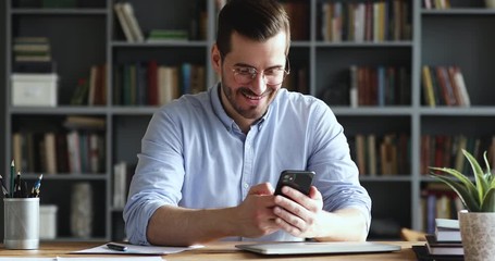 Wall Mural - Amazed happy businessman receiving sms message reading good news. Excited overjoyed male winner celebrating success looking at smart phone sitting at home office desk. Mobile victory concept