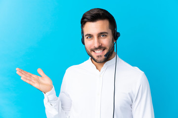 Poster - Telemarketer man working with a headset over isolated blue background holding copyspace imaginary on the palm