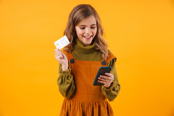 Wall Mural - Girl child isolated over yellow wall using mobile phone