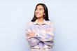 © luismolinero - Young Indian woman isolated on blue background looking up while smiling