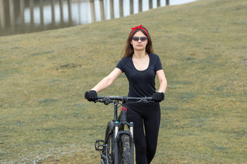 Girl on a mountain bike on offroad, beautiful portrait of a cyclist in rainy weather, Fitness girl rides a modern carbon fiber mountain bike in sportswear. Close-up portrait of a girl in red bandana.