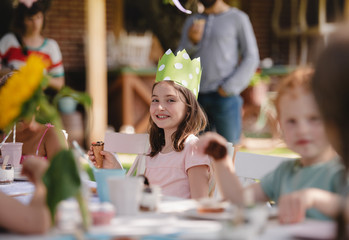 Small children sitting at the table outdoors on garden party, eating.