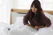 © amornchaijj - Asian woman is using her hands to hold her stomach because she has a stomach ache in bed room. Health care concept.