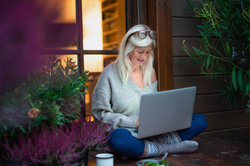 Wall Mural - Senior woman with laptop sitting outdoors on terrace, working in the evening.